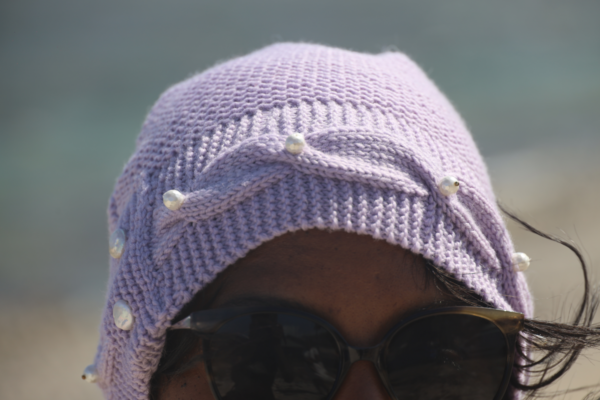 Un bonnet en laine lilas avec une bordure torsadée et des perles blanches sur le devant et deux perles sur l'arrière