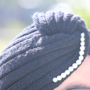 Une femme souriante porte un turban gris en cachemire tricoté main avec des perles sur le devant