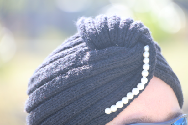 Une femme souriante porte un turban gris en cachemire tricoté main avec des perles sur le devant