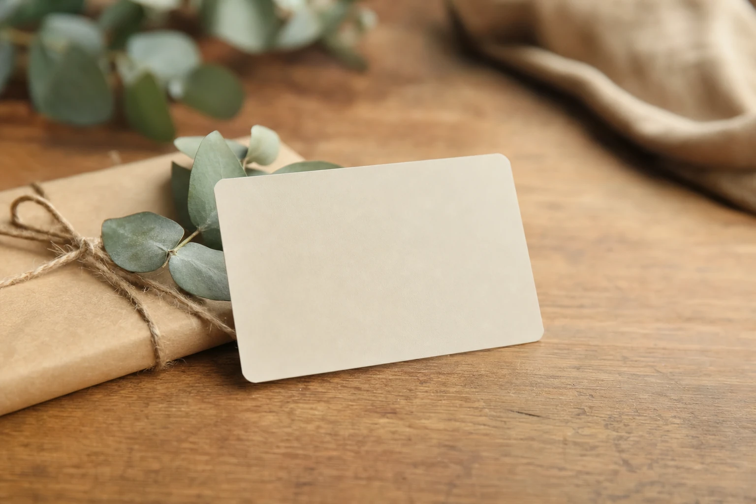 Une carte cadeau vierge posée sur une enveloppe en papier kraft avec un brin de végétal et de la ficelle naturelle