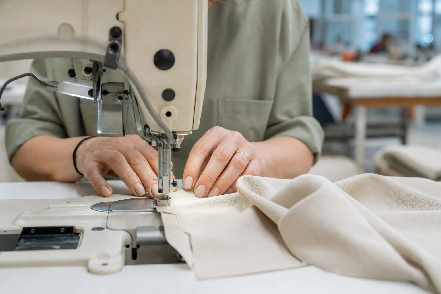 Mains d'une couturière guidant un tissu sous une machine à coudre industrielle dans un atelier de confection