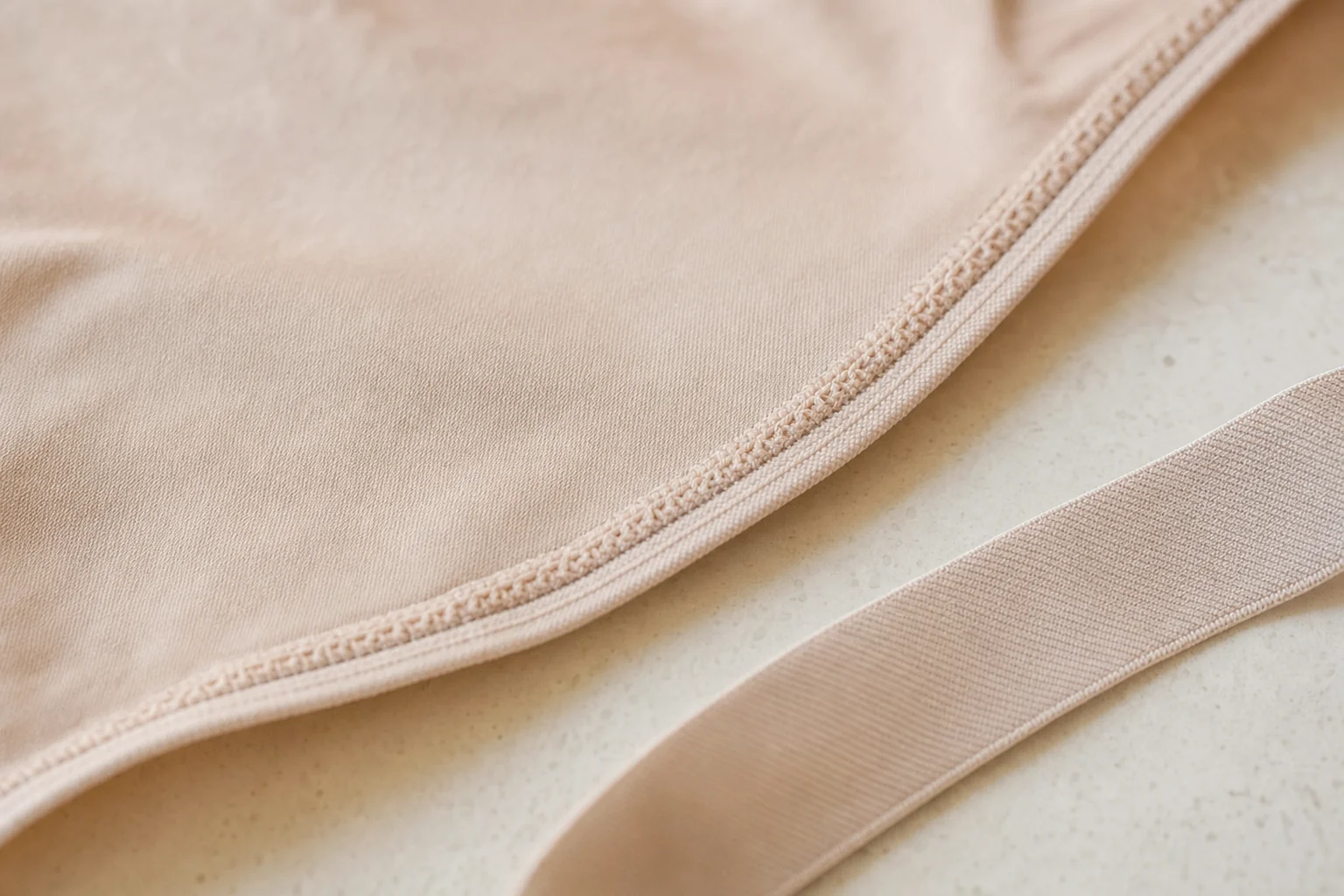 Détail rapproché d'une bande élastique et d'une couture plate sur une pièce de lingerie claire posée à plat sur un plan de travail